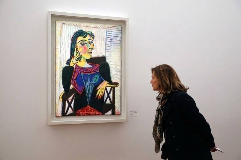 Woman viewing Picasso's colorful cubist portrait of Dora Maar hanging on a white gallery wall at the Musée Picasso in Paris