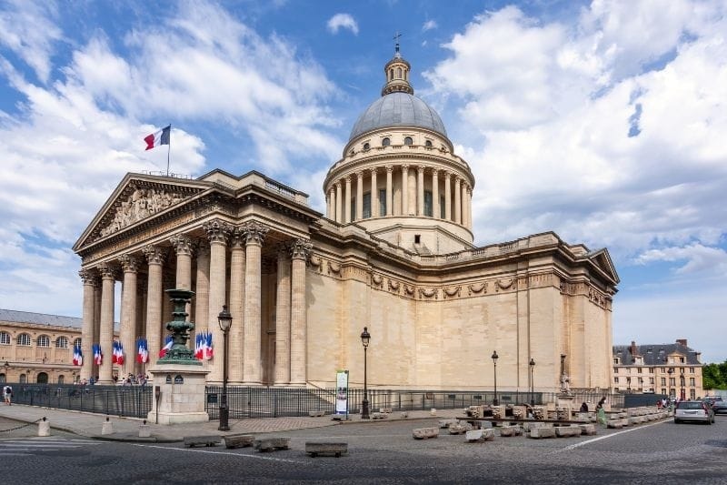 Exterior view of the Panthéon in Paris showing its large neoclassical dome, Corinthian columns, and French flag flying at the entrance
